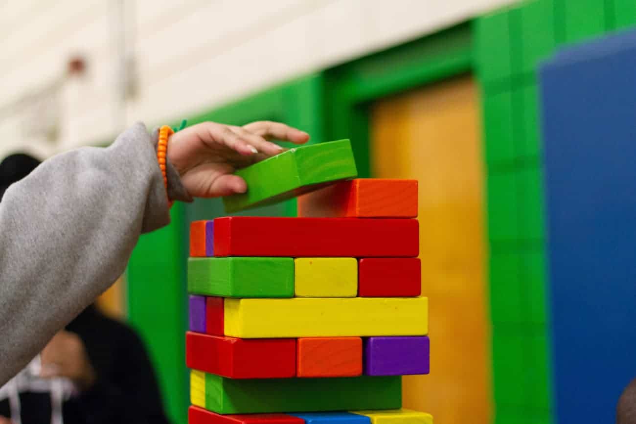 Main posant un bloc de bois vert au sommet d’une tour de blocs colorés