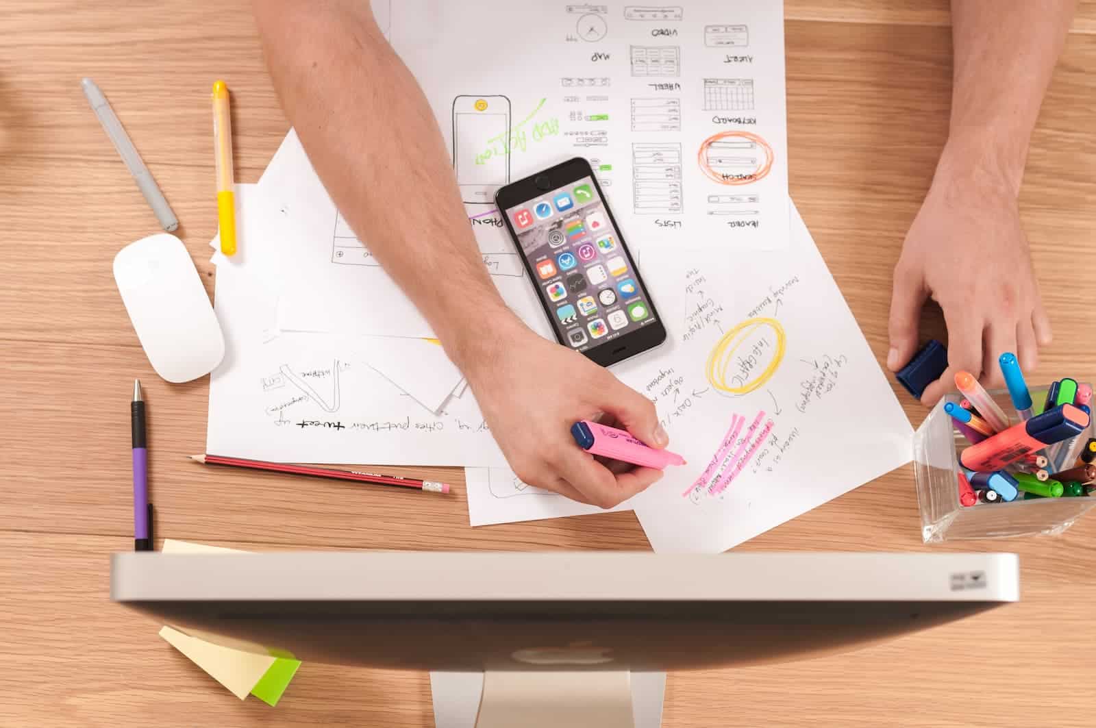 Hands annotating printed documents on a desk, next to a smartphone