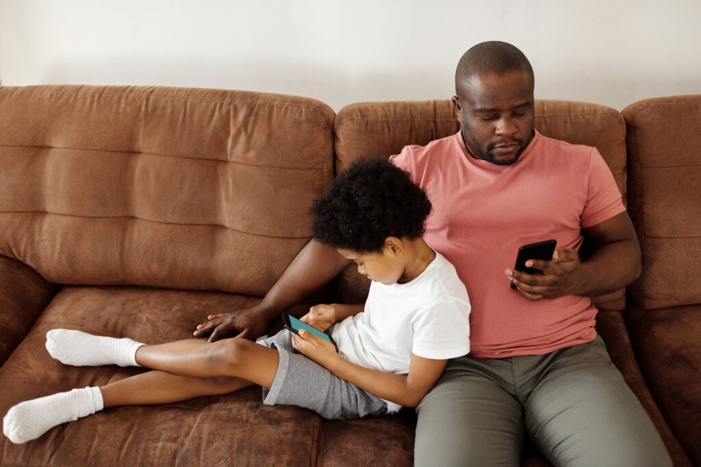 Père et fils assis sur un canapé, chacun absorbé par son smartphone